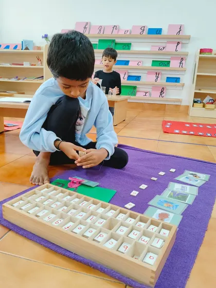 A child uses the Moveable Alphabet to build words. This language material allows children to express themselves in writing even before their hands are ready to form letters with a pencil, linking phonetic sounds to symbols in a tangible way.