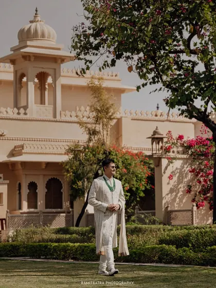 The groom stands in the lush gardens of The Oberoi Udaivilas, the magnificent palace providing a regal backdrop.