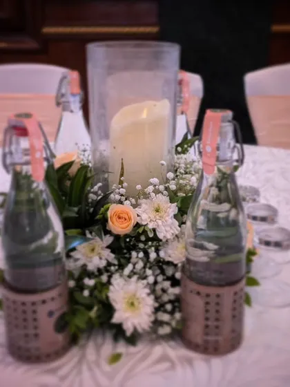 A charming and rustic table centerpiece, with a central candle surrounded by small flowers and greenery, perfect for an intimate and relaxed celebration.