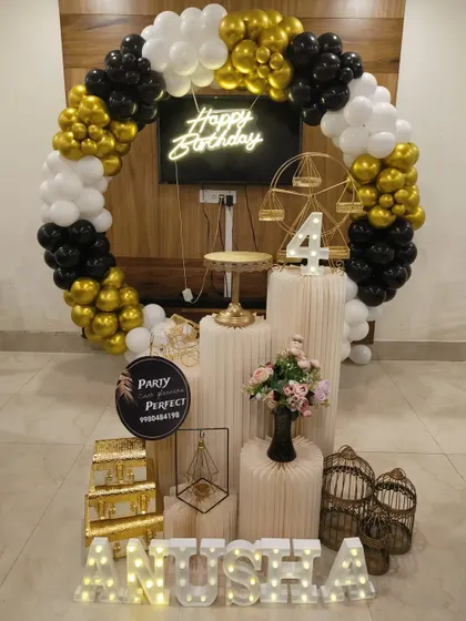 A classic black, white, and gold theme is always a stylish choice for any age. This decoration includes a full balloon ring, a central neon 'Happy Birthday' sign, a light-up number '4', and multiple pedestals for the cake and other decorative elements like a miniature Ferris wheel.