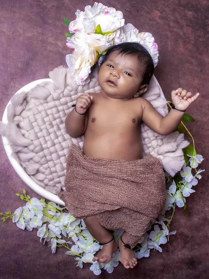 An awake baby boy lies in a heart-shaped bowl, looking up with curiosity. This pose shows a different side of newborn photography, focusing on their alert expressions.