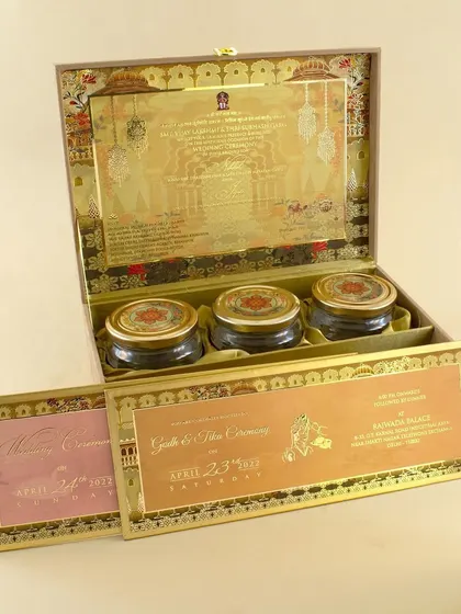 This opulent invitation box features intricate gold foil work on the inside lid and a velvet-lined interior. It holds multiple inserts and three matching gift jars, making it a truly luxurious announcement.