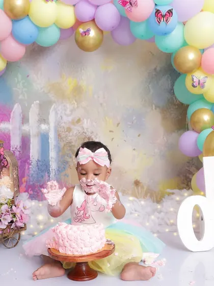 With cake-covered hands and a happy smile, this one-year-old is fully enjoying her cake smash session. This shot captures the messy, joyful reality of a first birthday.