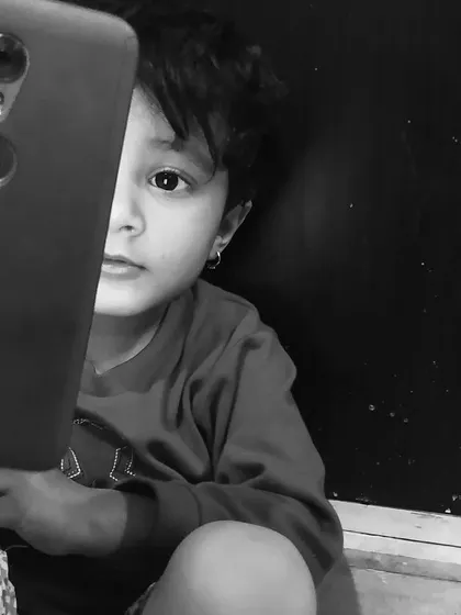 A black and white portrait of a child peeking from behind a phone. This series explores how technology is a part of modern childhood, captured in a timeless monochrome style.