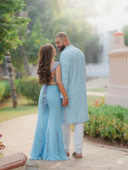 A candid shot from behind as a couple walks through a garden path during their Haldi celebration. This photo highlights the beautiful details of the bride's outfit and captures a quiet, in-between moment.
