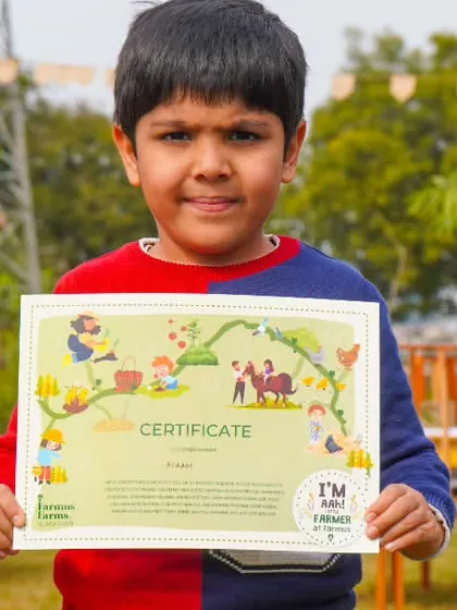 A young boy proudly holding his 'Friend of Farmus' certificate after completing the farm activities.