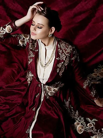 An artistic top-down shot where the model is enveloped by the deep red fabric of her outfit. This perspective creates a visually rich and textured image, focusing on the details of the embroidery.
