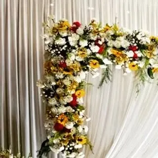 A corner detail of a floral arch, showing a mix of sunflowers, red roses, and white chrysanthemums. This vibrant combination is perfect for a joyful and colorful celebration.