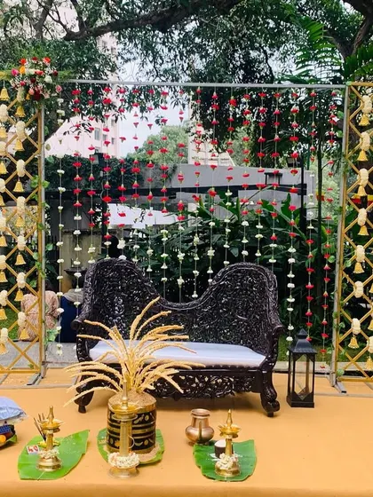 A simple yet elegant outdoor stage for an engagement. The decor features a traditional carved sofa, hanging flower curtains, and side panels with hanging bells for an authentic touch.