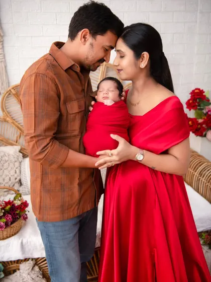A portrait capturing the profound love of new parents, both gazing at their newborn wrapped in a vibrant red swaddle. This image embodies the beginning of a family's story, a moment of pure connection and adoration that we specialize in preserving.