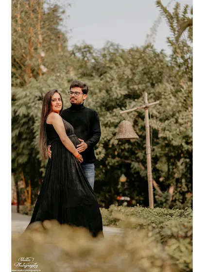 A classic pose for a couple's maternity portrait, taken in a lush green park. The image is simple, elegant, and full of warmth.