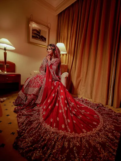 A full portrait of a bride in her magnificent red lehenga with a long train. My goal is to ensure your makeup looks stunning from every angle, complementing the grandeur of your bridal outfit.
