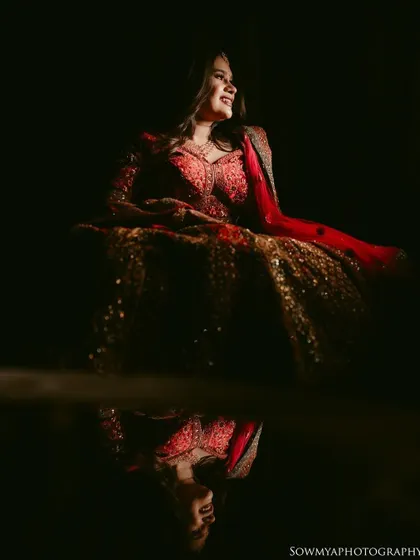 A dramatic portrait of a bride in her red lehenga, with her reflection captured on a glossy surface below. The play of light and reflection is stunning.