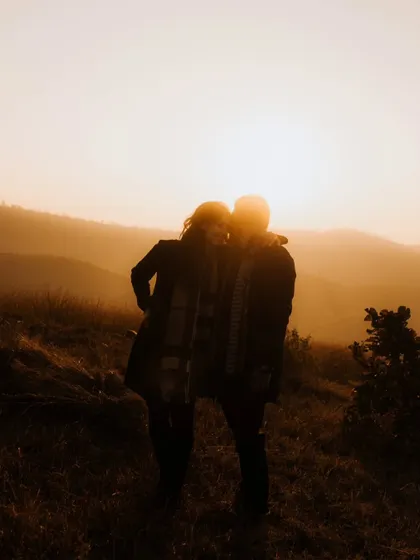 A soft, warm silhouette of the couple against the hazy, golden sunset. This artistic shot is filled with romance and a sense of peaceful intimacy.