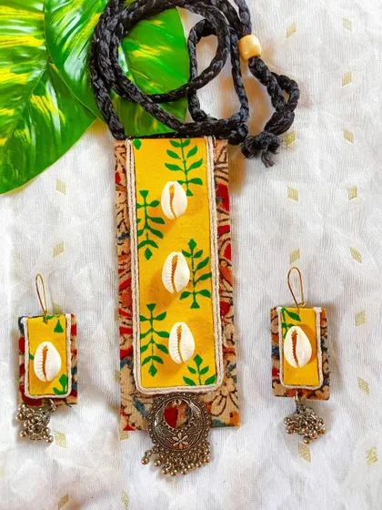 This fabric necklace combines Kalamkari print with hand-painted details and cowrie shells. The German silver charm at the bottom adds a bohemian touch.