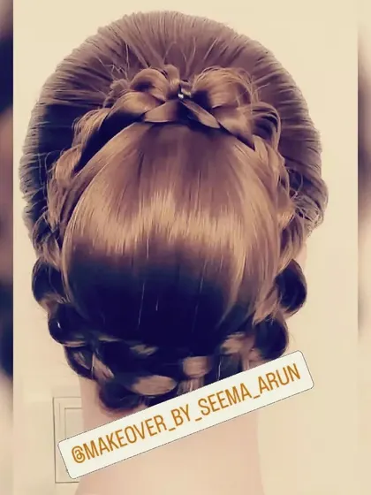 A polished and neat bun hairstyle with a unique braided detail on top that resembles a bow. This is a chic and modern take on the classic updo, great for a sleek and stylish look.