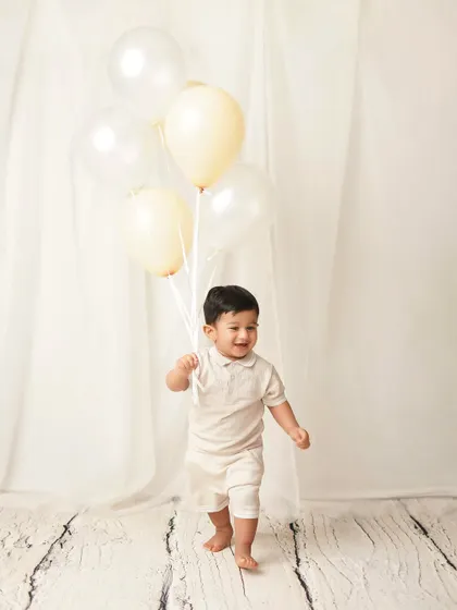 A little boy takes his first steps, holding a bouquet of balloons. This is a huge milestone, and a photoshoot is a wonderful way to celebrate it.