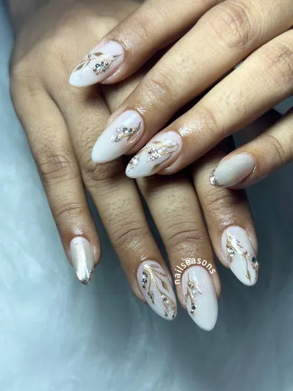 An elegant white manicure with hand-painted gold and silver leafy vines, accented with sparkling rhinestones.