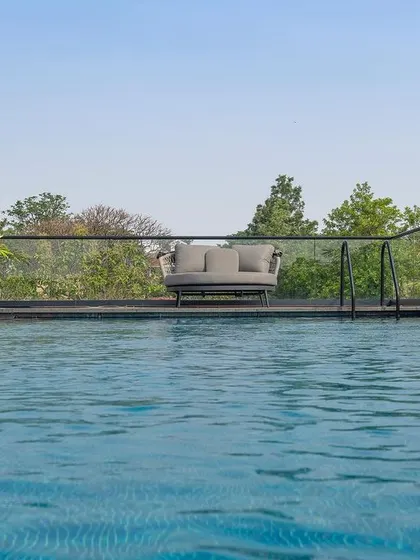 A view across a tranquil swimming pool towards a comfortable seating area on the far side. The landscape is kept minimal, with the expanse of water and the surrounding trees creating a peaceful atmosphere.
