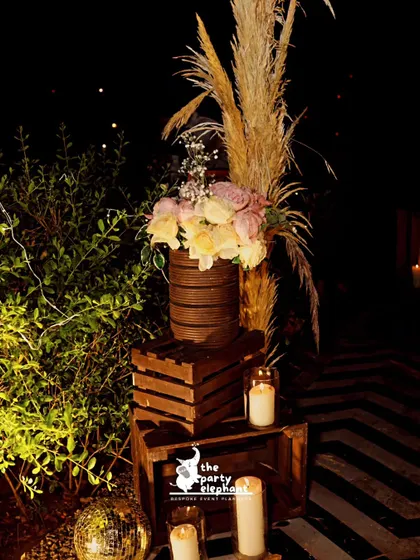 A close-up of the decor details, showing a mix of dark wood crates, pampas grass, floral arrangements, and candles, which together created a sophisticated, rustic-luxe aesthetic.