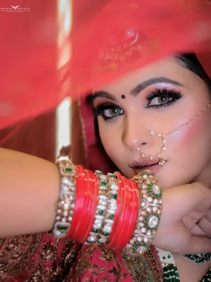 A close-up shot focusing on the bride's eyes, framed by her red veil and bangles. The composition is tight and impactful, highlighting her expressive look.