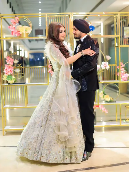 A full-length portrait of the Sikh couple at their engagement. The bride's flowing silver gown and the groom's classic black tuxedo create an elegant and timeless image.