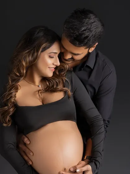 An intimate and loving embrace. This close-up shot captures the couple in a tender moment, their expressions soft and happy, set against a classic dark studio background.