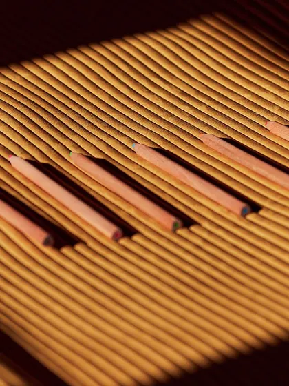 An abstract view of the 'Colonne' wallcovering, with colored pencils resting in its grooves. This creative shot emphasizes the design's deep, tactile, and three-dimensional quality.