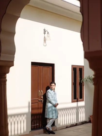 A stylish portrait of the groom, framed by an archway, as he stands against a white wall with interesting shadows creating a dynamic composition.