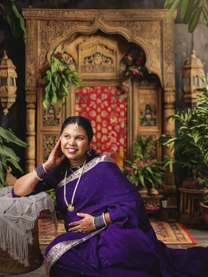 Celebrate your heritage with a traditional maternity photoshoot. This portrait, inspired by classic Indian artistry, features a rich purple saree and an ornate, traditional backdrop, creating a timeless and culturally significant memory.