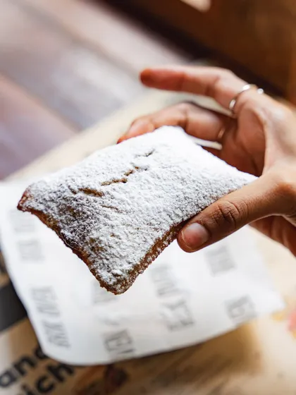 A hand holding up a freshly fried sourdough beignet. They are crispy, pillowy, and incredibly addictive.