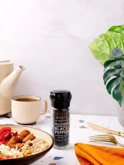 A clean and crisp lifestyle shot of Tellicherry Black Pepper. The modern, bright lighting and minimalist props highlight the premium quality of the spice for a discerning customer.