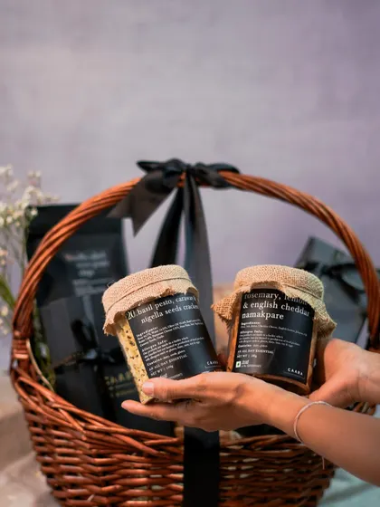 Choosing the perfect gift is easy with our customisable hampers. Here, we are holding jars of our popular basil pesto and rosemary namakpare, ready to be added to a bespoke wicker basket hamper.