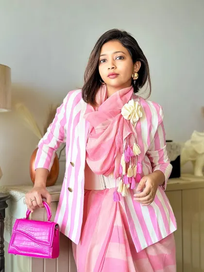 A close-up of the blazer and saree combination. The rosette adds a soft, textural element to the sharp lines of the stripes.