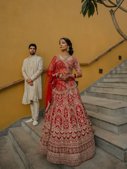 A regal portrait of the couple in their stunning red and cream wedding attire. We use architectural elements like staircases to add a touch of grandeur to our compositions.
