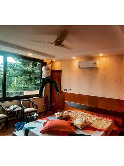 The same bedroom during the final installation phase. Our team is seen giving the finishing touches, with the bed, wooden headboard, and new wallpaper already in place.