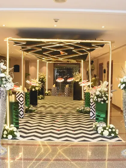 A modern and geometric entranceway with a black and white chevron floor. The golden frame structure and tall silver vases with white flowers add a touch of sophistication to the graphic design.