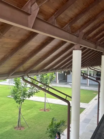 A view from an upper-level corridor at Vellore International School, looking down onto a green courtyard. The sloping wooden roof provides shade and a sense of warmth.