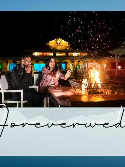 A wider shot of the bonfire scene, capturing the full ambiance of the location. The sparks flying into the night sky add a dynamic and magical element to this romantic pre-wedding moment.
