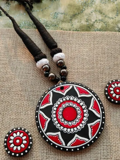 A simple and elegant necklace set with a round pendant featuring a beautiful 'alpona' and mandala design in red, black, and white.