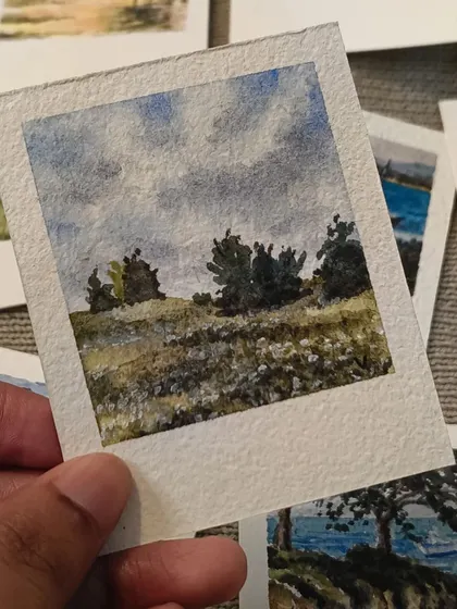 A field of wildflowers under a cloudy sky, painted in a soft, impressionistic style. This mini Polaroid captures the feeling of a breezy, overcast day in the countryside.
