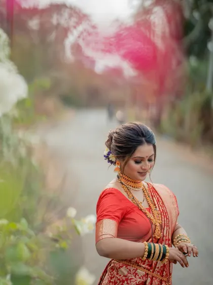 A dreamy, artistic portrait of a bride in a red saree, with a soft focus and natural elements framing the shot.