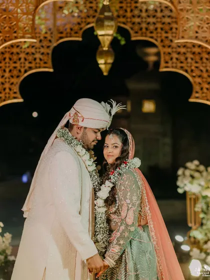 A quiet moment together after the rituals. The warm lighting and intricately carved golden arches of the mandap create a romantic and intimate backdrop for the newlyweds' first portraits as a married couple.
