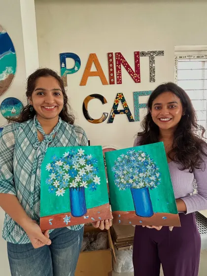 Two friends with their matching paintings of blue flowers in a vase.