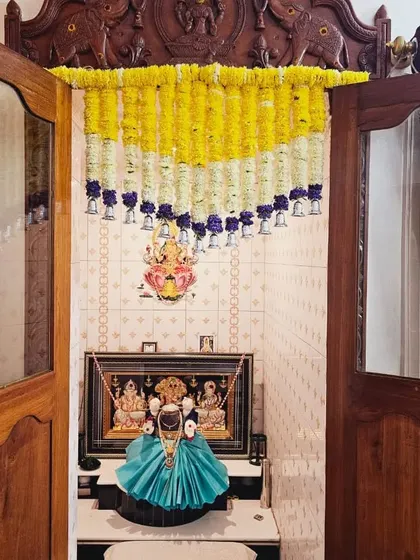 A Varamahalakshmi festival setup with the pooja unit decorated with yellow and purple flower garlands.