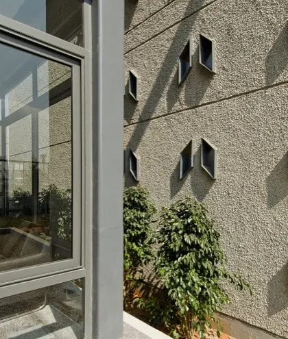 A detailed view of the building's facade, showing the interplay between the textured concrete surface and the uniquely shaped, recessed windows. This detail adds depth and character to the exterior, creating dynamic shadow lines throughout the day.