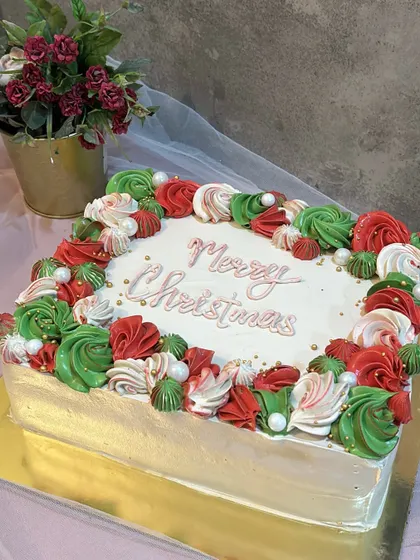 A festive Merry Christmas cake with red, green, and white buttercream swirls, decorated with edible pearls.