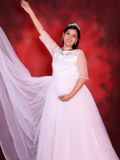 An elegant maternity shot of a woman in a white gown, with the long trail flowing behind her.