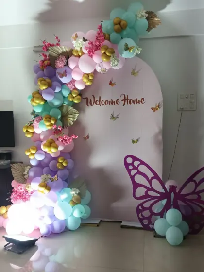 A whimsical butterfly-themed welcome home setup. The pastel rainbow balloon arch is decorated with gold butterflies and cherry blossoms, with a large butterfly cutout adding a beautiful touch to the arrangement.