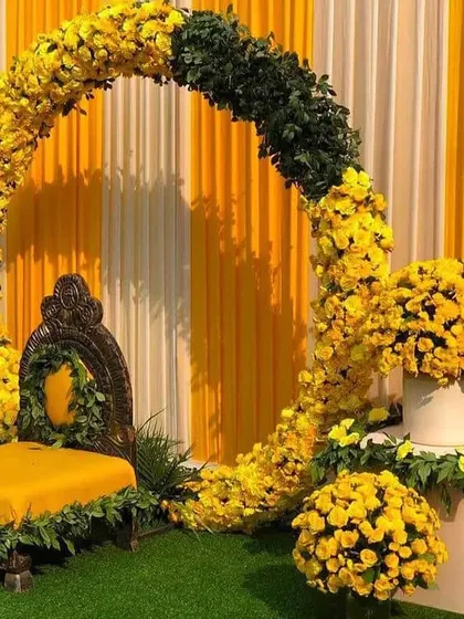 A modern Haldi decor featuring a floral ring of yellow marigolds against a backdrop of yellow and white striped curtains.